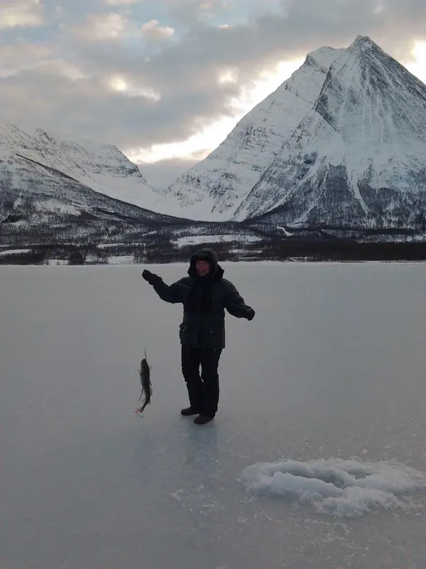 A guest holding up a fish on the frozen lake