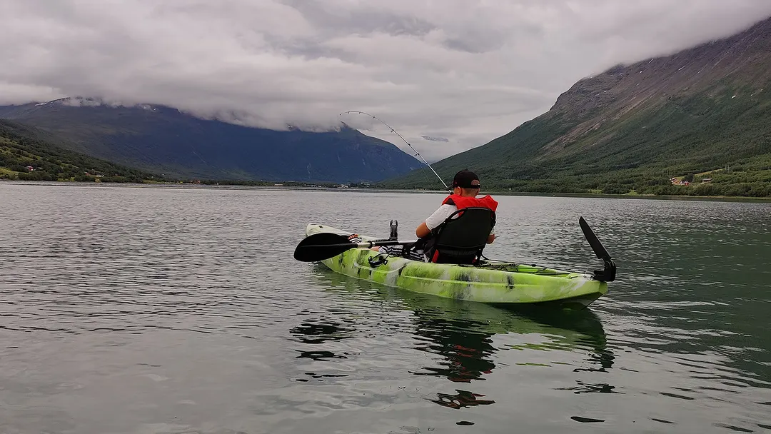 A guest fishing from a kayak on a grey summer fjord
