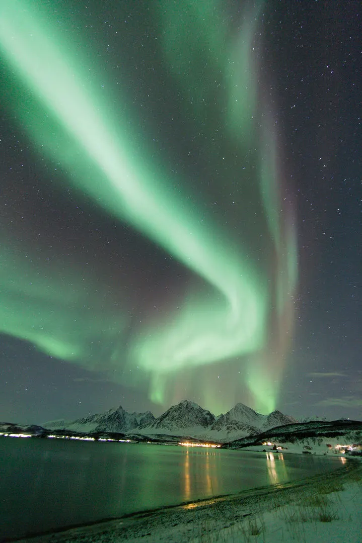 A green aurora curling above a moonlit valley